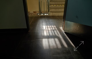 Offene Tür mit Sonnenlicht, das durch ein Fenster auf den dunklen Boden fällt.