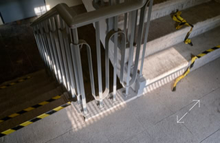 Treppenabsatz mit Metallgeländer, gelb-schwarzem Absperrband und Schattenwurf.