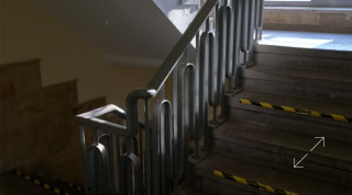 Treppenhaus mit Metallgeländer und gelb-schwarzen Markierungen auf den Stufen.