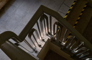 Blick von oben auf ein Treppenhaus mit Metallgeländer und gelb-schwarzen Warnstreifen an der Seite.